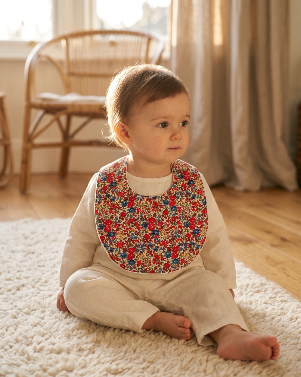 Bébé assis sur un tapis, portant le bavoir Liberty rouge et bleu